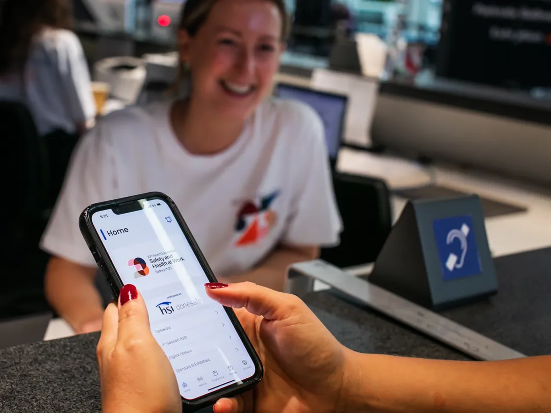 Delegate holding a phone with the event app open, lanyard visible, at a registration desk